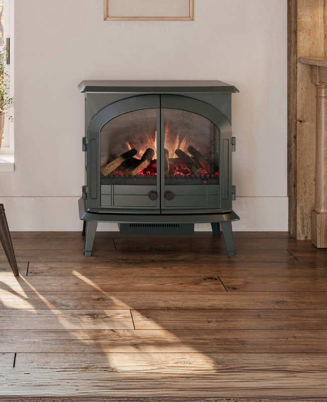 Classic-style electric fireplace stove by Modern Ember with arched glass doors and glowing log set, placed in a cozy farmhouse interior with wood floors and neutral walls.