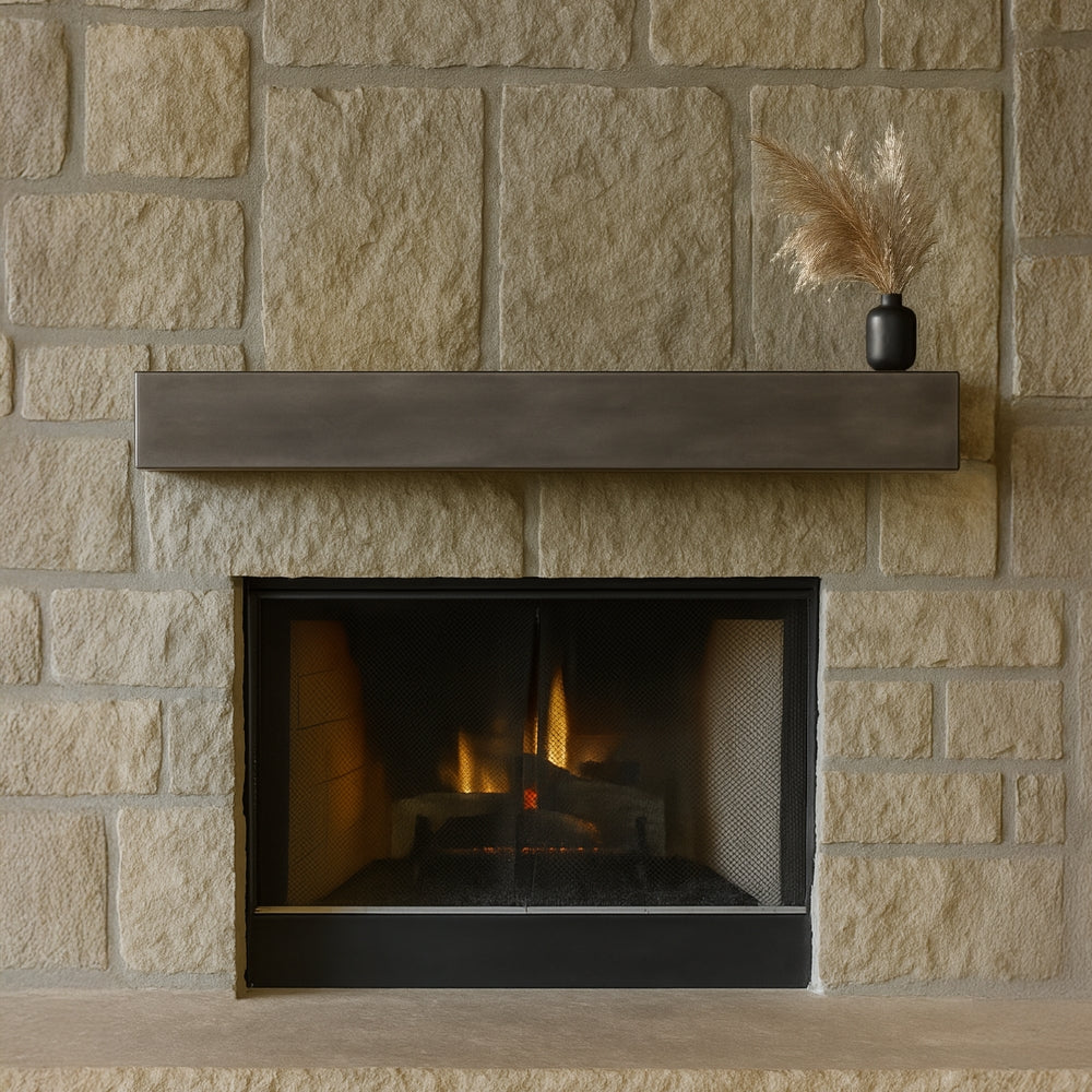 Lustra Metal Mantel Shelf in Forged Iron mounted on a large, rustic tan stone fireplace, showcasing contrast between metal and stone.