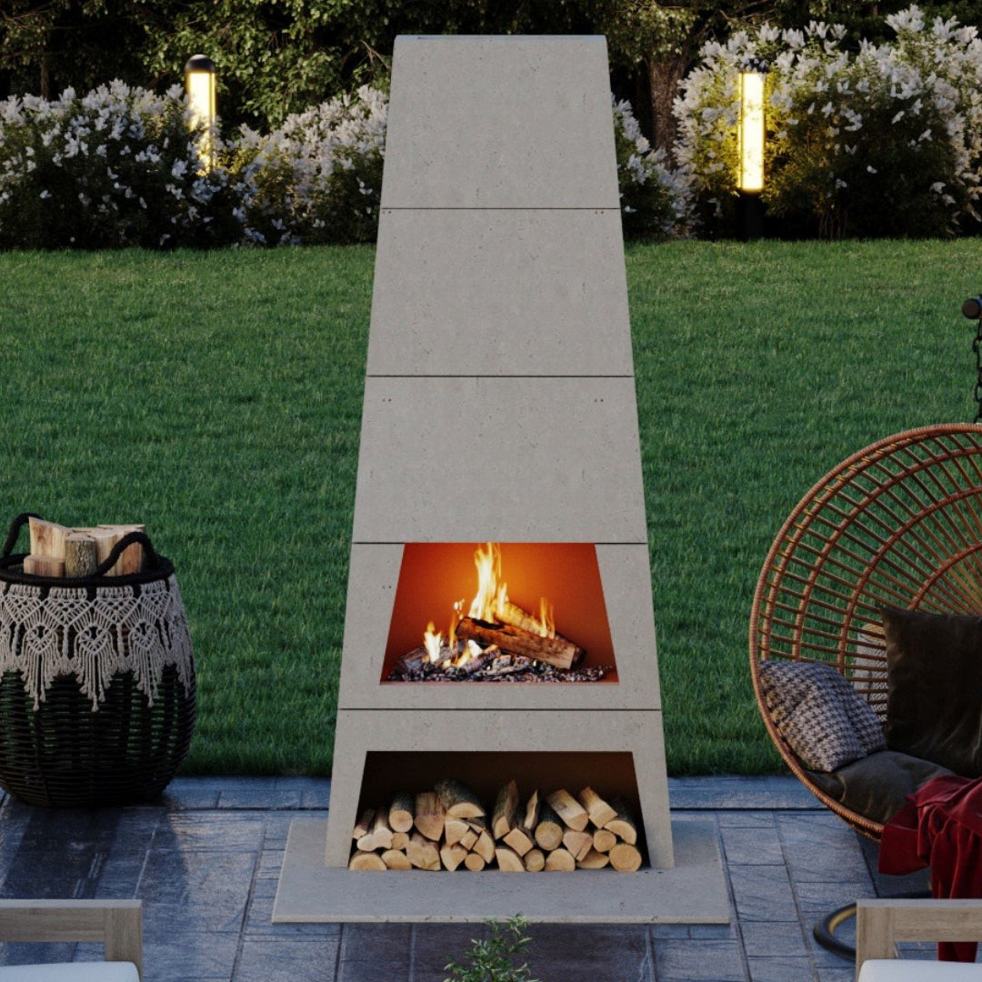 Kairo Outdoor Woodburning Fireplace in a Limestone finish on a patio, showcasing its bold trapezoid shape and logs stored beneath the firebox.