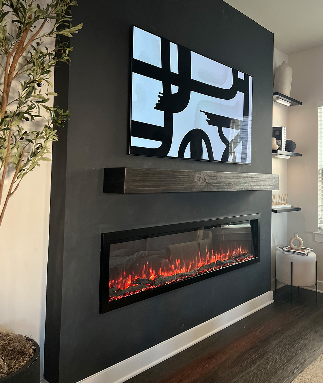 "Modern Ember electric fireplace professionally installed in a sleek black accent wall with wood mantel and mounted art display, illustrating architect precision and stylish modern design integration