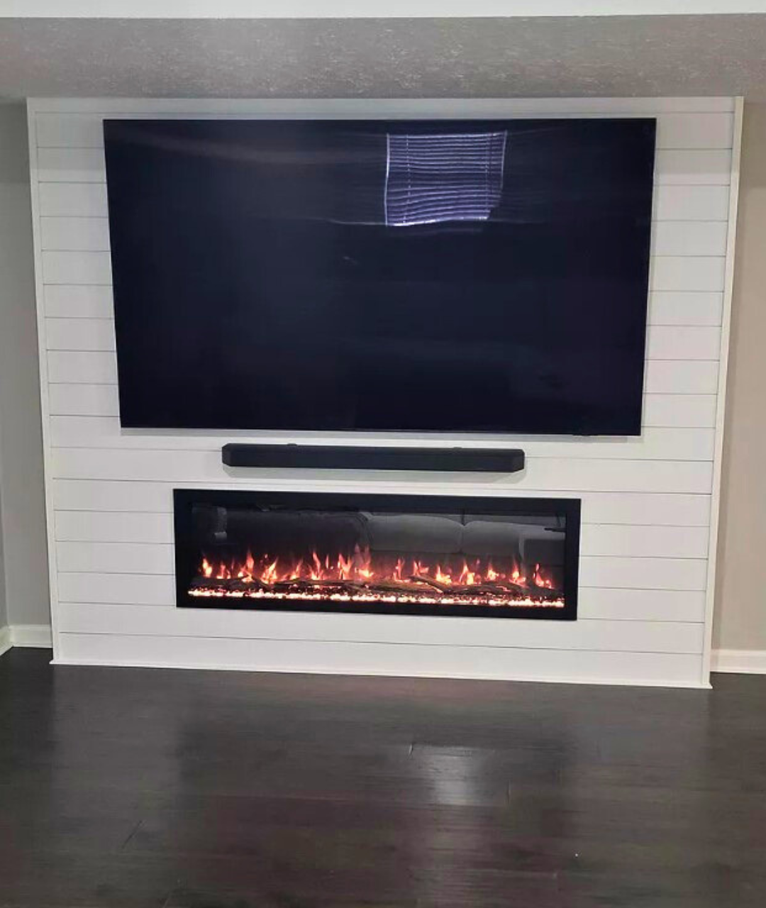 Modern Ember electric fireplace installed in a white shiplap feature wall beneath a mounted TV and soundbar, showcasing perfect for developers looking for craftsmanship and modern styling.