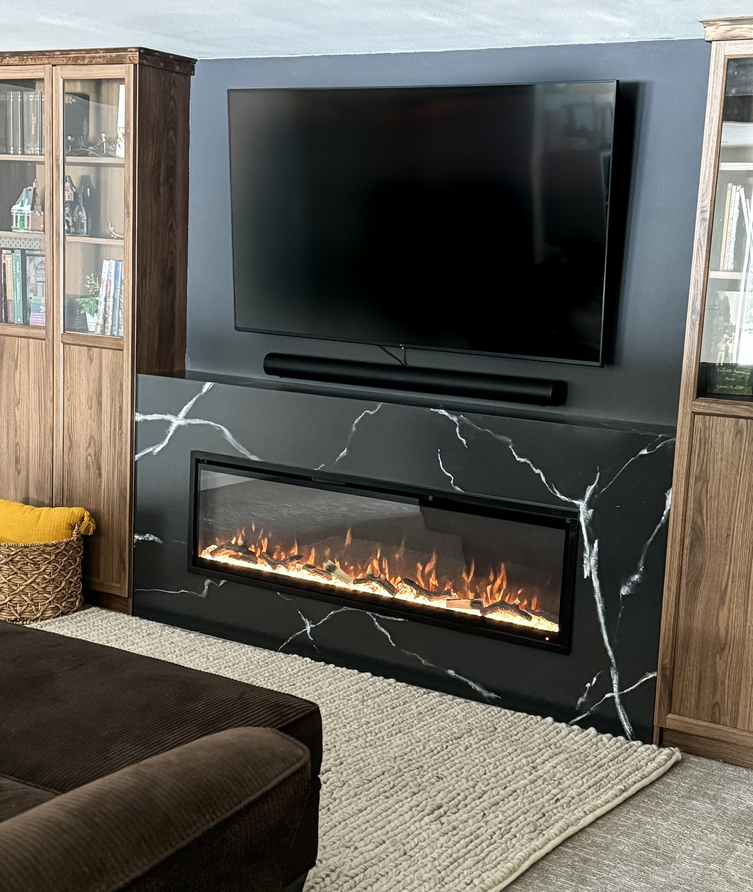 Custom installation of a Modern Ember electric fireplace set in a black marble-look feature wall with mounted TV and wood built-ins, demonstrating premium craftsmanship trusted by trade professionals.