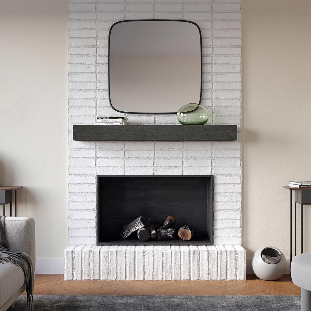 Alpine 60-inch Concrete Mantel Shelf in Ember finish, mounted on a white painted brick fireplace with a square mirror, stacked books, and a green glass vase, styled in a modern living room.