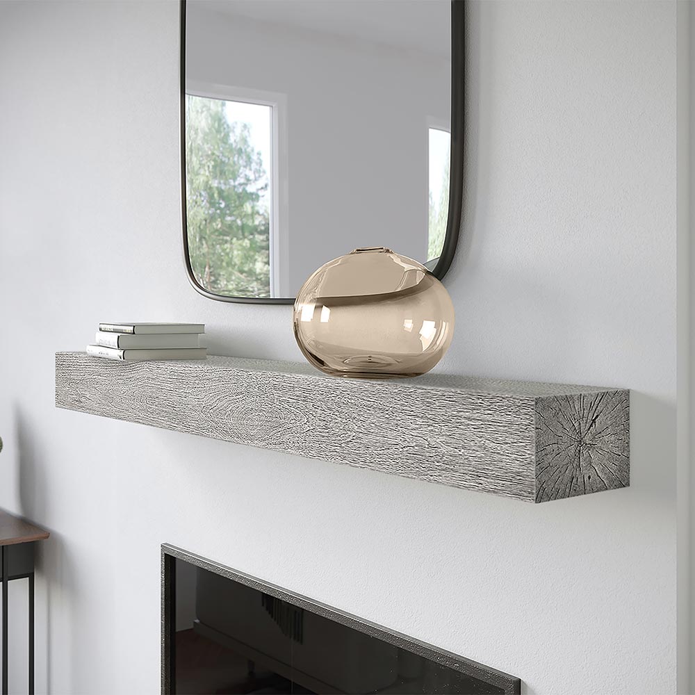Alpine 60-inch Concrete Mantel Shelf in Fog finish, mounted above a modern fireplace with a decorative glass vase and stacked books, showcasing its textured woodgrain design and clean lines.