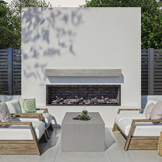 Alpine 60-inch Concrete Mantel Shelf in Fog finish, installed on an outdoor modern fireplace surround, styled with cushioned wooden lounge chairs and a concrete coffee table in a contemporary patio setting.
