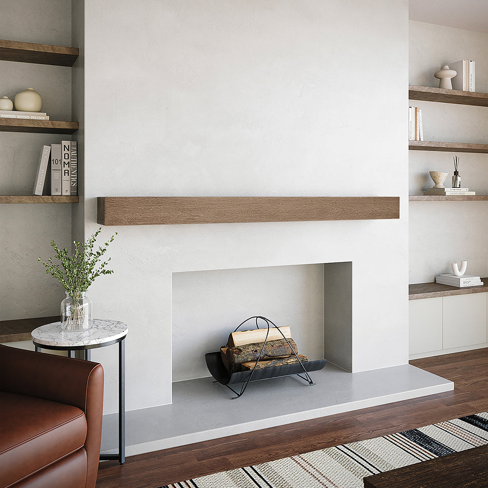 Alpine 60-inch Concrete Mantel Shelf in Grove finish, installed on a minimalist white fireplace surround with built-in shelving, styled with books, pottery, and greenery for a warm modern living room design.