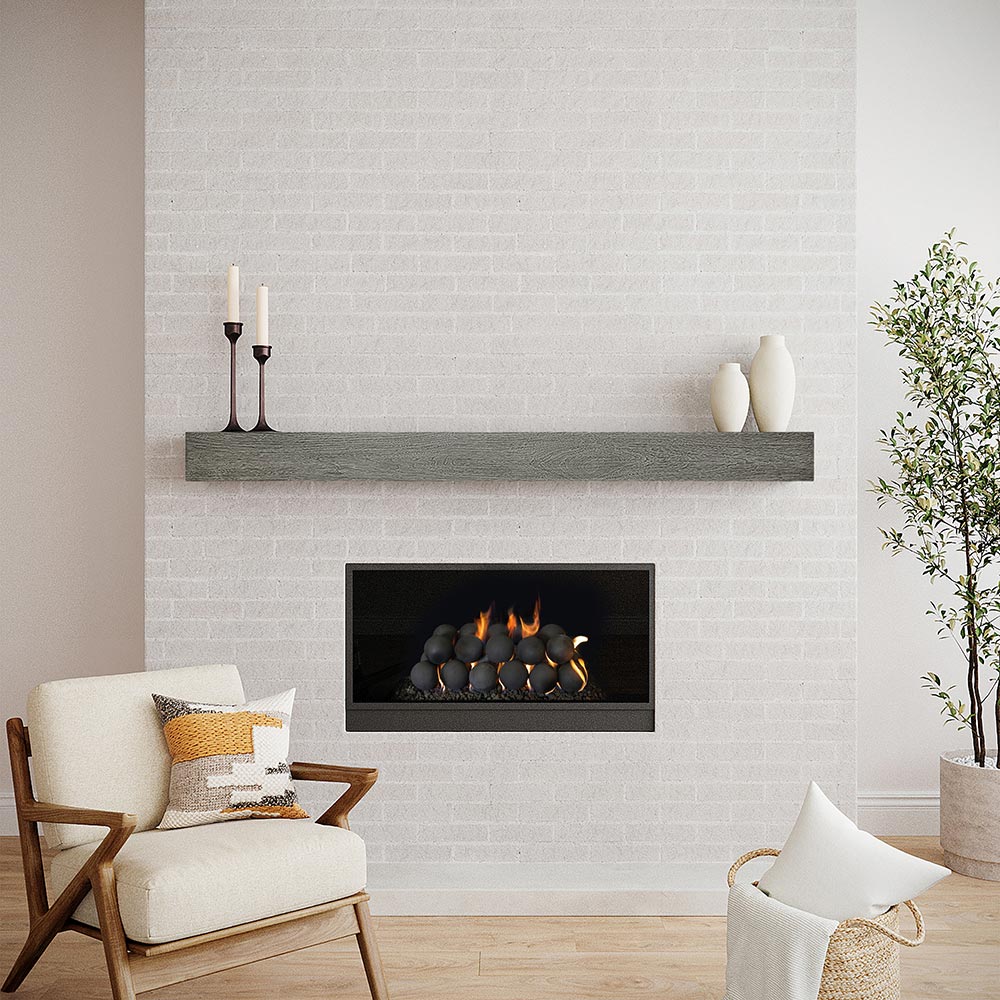 Alpine 60-inch Concrete Mantel Shelf in Ash finish, installed on a white brick fireplace wall, styled with candlesticks and ceramic vases, in a modern living room with a wood-frame accent chair and gas fireplace.