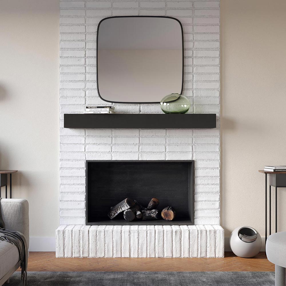 Everett 60-inch Concrete Mantel Shelf in Carbon finish, mounted on a white painted brick fireplace with a square mirror, stacked books, and a green glass vase, styled in a contemporary living room.