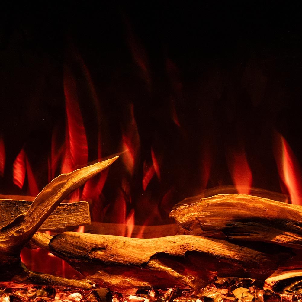 A close-up view of the Highmark Traditional electric fireplace effect with glowing red and orange flames rising behind stacked wood logs and embers against a dark background.