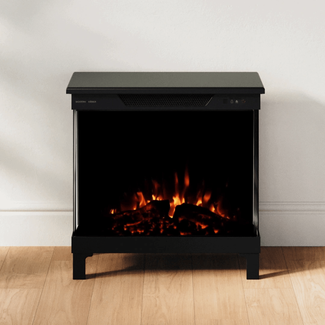 A black electric fireplace with glowing orange and yellow faux flames, set against a plain white wall on a light wood floor.