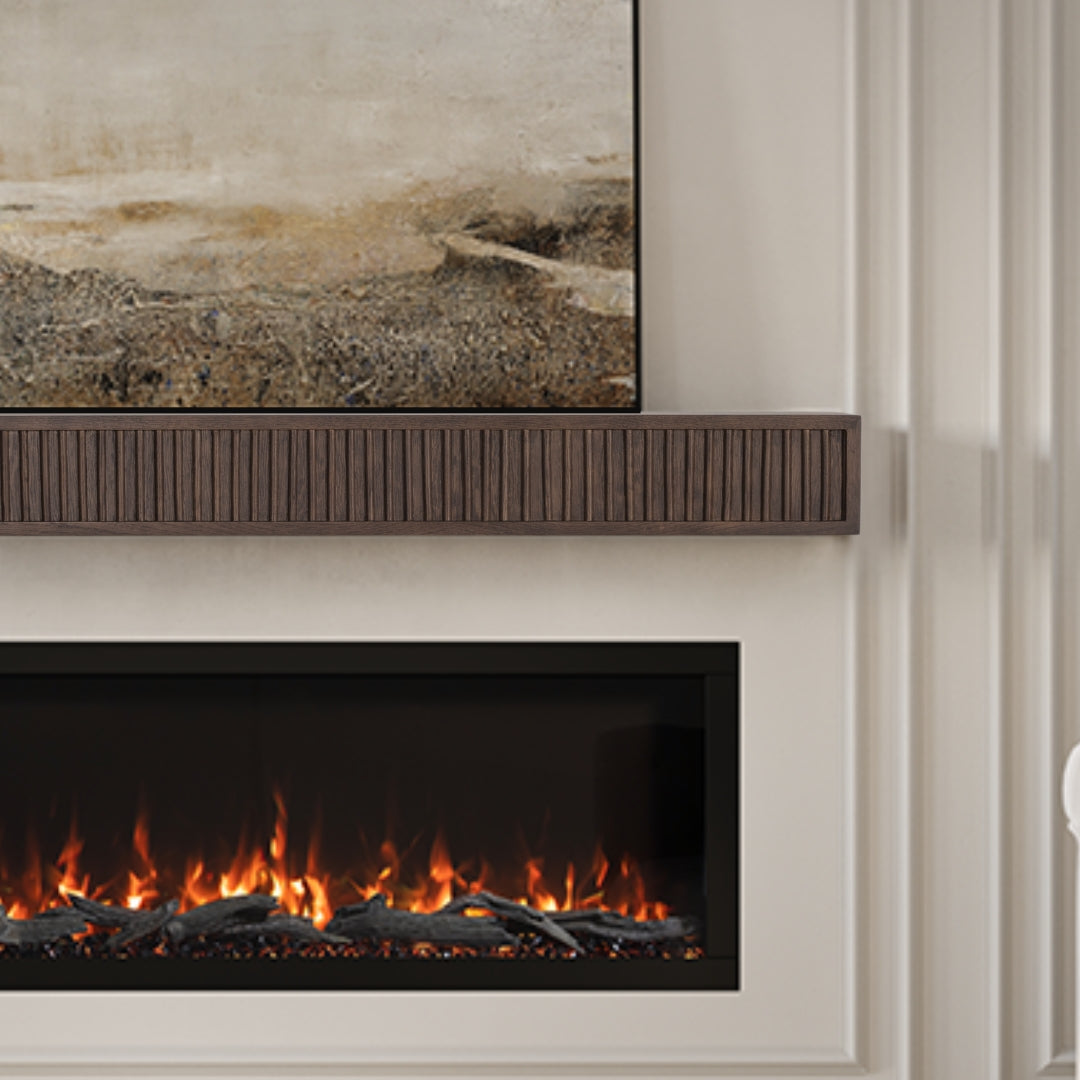 Modern Ember Monti Boxframe fluted mantel shelf in a dark brown wood called Sabel installed above a flaming electric fireplace, with a simple painting above. Contemporary living room style.