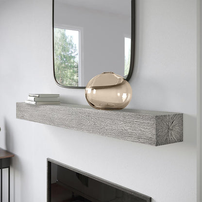 Alpine 60-inch Concrete Mantel Shelf in Fog finish, mounted above a modern fireplace with a decorative glass vase and stacked books, showcasing its textured woodgrain design and clean lines.