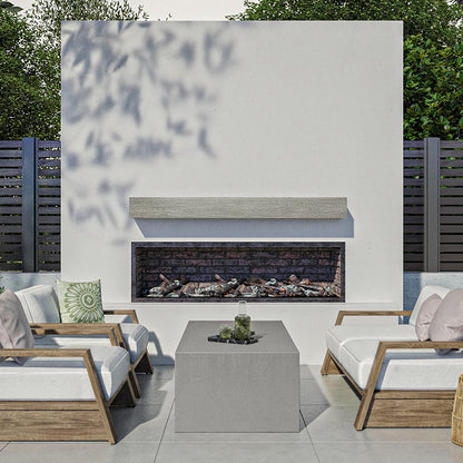 Alpine 60-inch Concrete Mantel Shelf in Fog finish, installed on an outdoor modern fireplace surround, styled with cushioned wooden lounge chairs and a concrete coffee table in a contemporary patio setting.