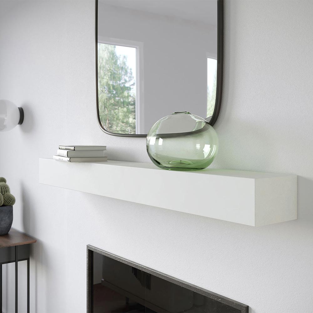 Angled view of Everett 60-inch Concrete Mantel Shelf in white Linen finish, mounted on a white wall fireplace with a square mirror, stacked books, and a green glass vase.