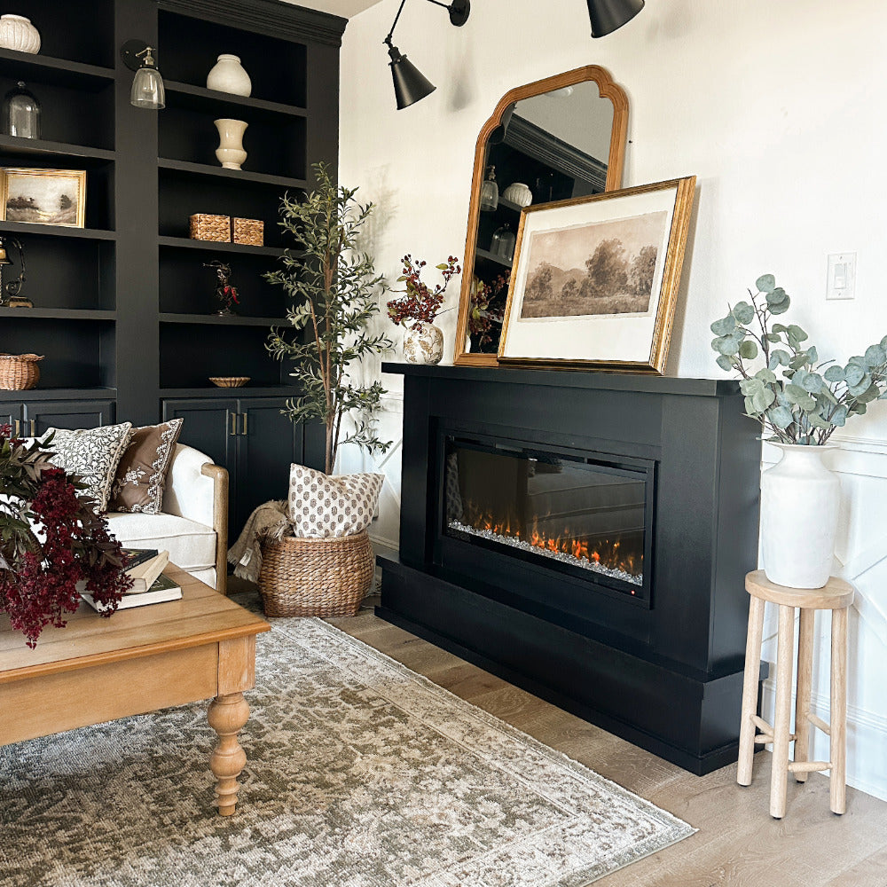 The black Patton Electric Fireplace Mantel Package with a mirror and frame propped on top, in a customers living room.