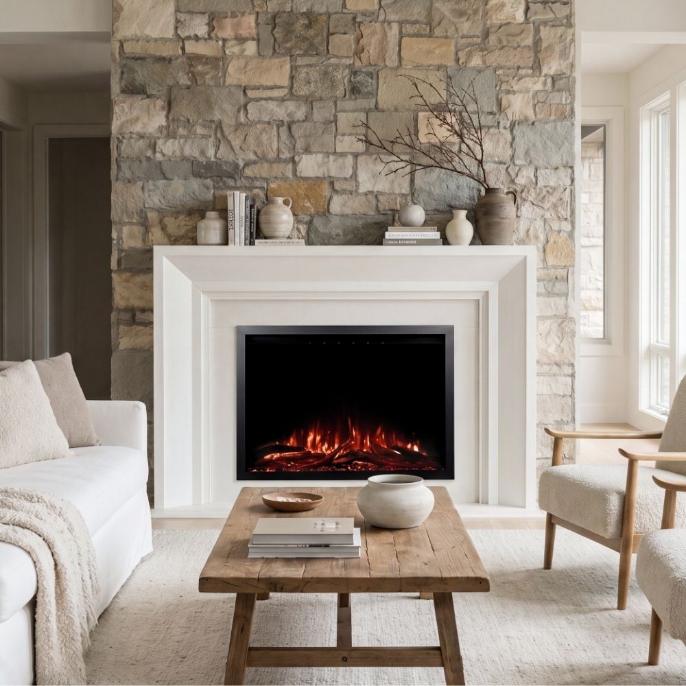 A modern electric fireplace with glowing orange and red faux logs, set within a white mantel and a rustic stone wall, in a bright, contemporary living room.
